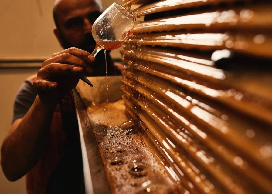 Man pours liquid from a glass over a tiered structure, creating drips and bubbles in an indoor setting with dark lighting.