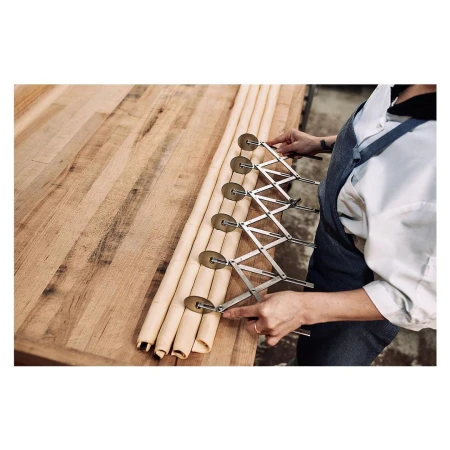 Baker using an expandable dough divider to cut rolled dough on a wooden surface, close-up view, highlighting precision in food preparation.
