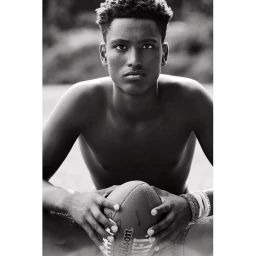 Black and white portrait of a young man holding an American football with wristbands.