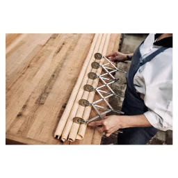 Chef in white coat and denim apron using a multi-wheel pastry cutter on rolled dough on a wooden workbench