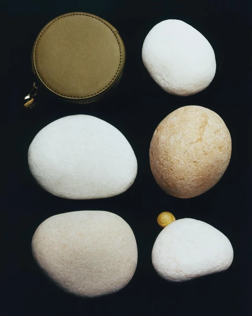 Overhead still life: A round, olive-green zippered case and five smooth, light-colored stones are set against a dark backdrop.
