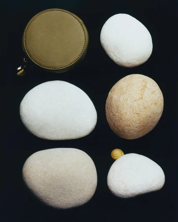 Overhead still life: A round, olive-green zippered case and five smooth, light-colored stones are set against a dark backdrop.