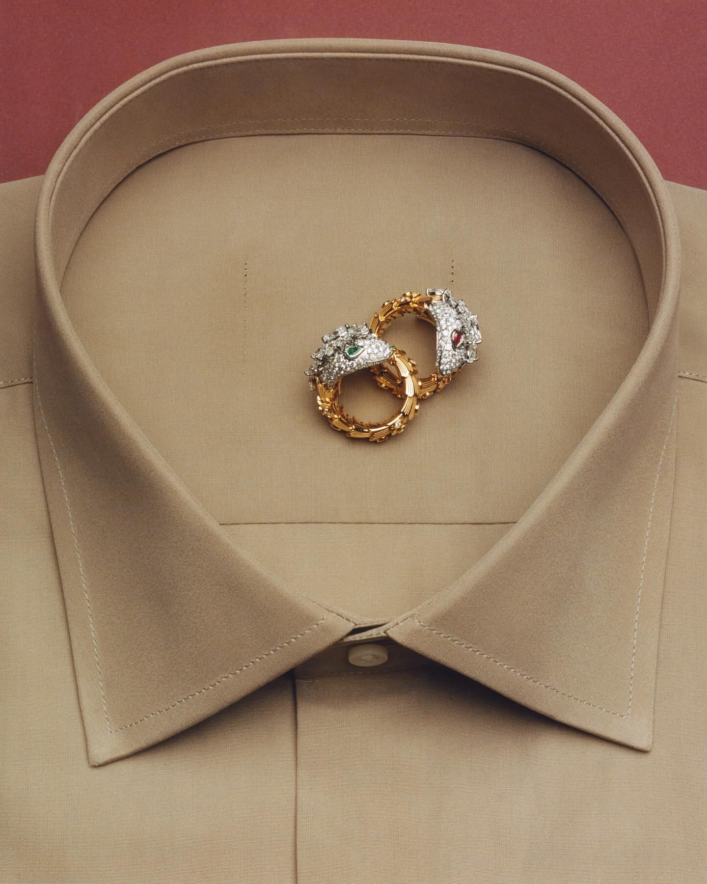 Two ornate gold and diamond snake rings resting inside the collar of a beige dress shirt photographed by Charles Negre