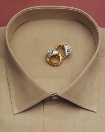 Two ornate gold and diamond snake rings resting inside the collar of a beige dress shirt photographed by Charles Negre