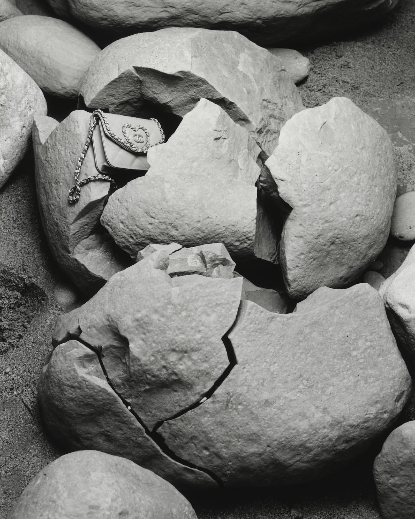 Monochrome still life of a purse nestled inside broken stone fragments, set against a rough gravelly background in a close-up shot.