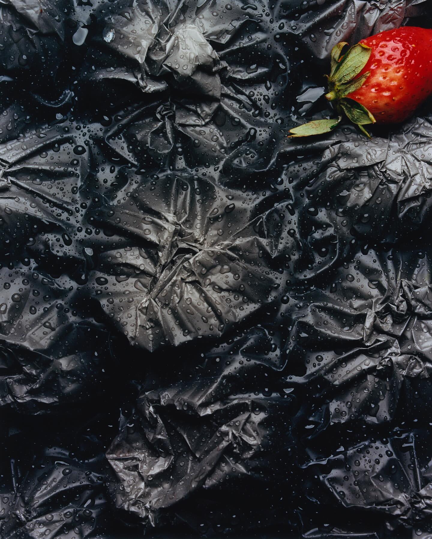 Close-up of a fresh red strawberry with green leaves against a dark, heavily textured background covered with water droplets.