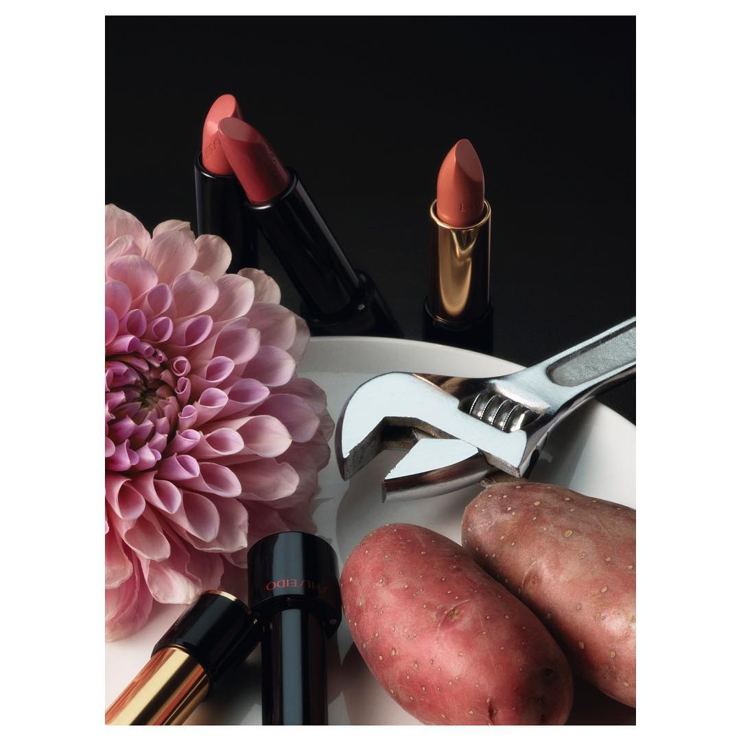 Still life shot with beauty and food themes featuring lipsticks, potatoes, dahlia on a white plate, set against a dark background.
