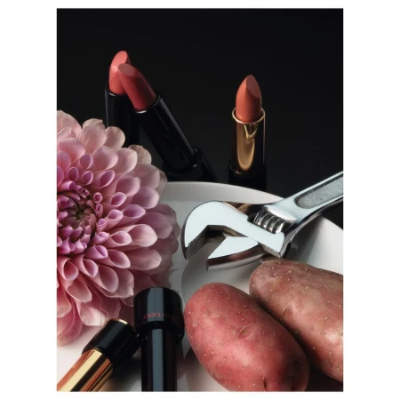 Still life shot with beauty and food themes featuring lipsticks, potatoes, dahlia on a white plate, set against a dark background.