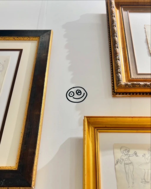 A simple black line drawing of a smiley face on a white wall, framed by ornate gold and dark wood picture frames.