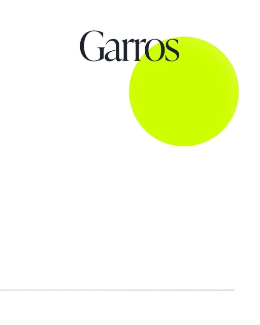 A tennis ball, brightly lit, sits near the word 'Garros' on a clean white surface, creating a stark, minimalist composition.