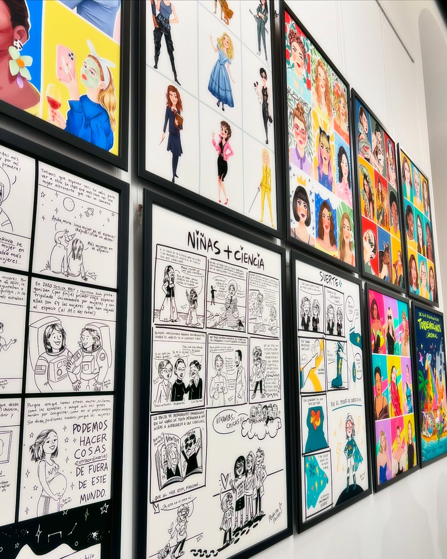 Wall display of framed art featuring cartoon and illustrated drawings in a brightly lit indoor setting.