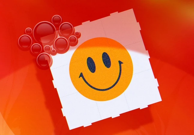 Orange smiley face on a white tile pattern against an orange background with red transparent spheres in the upper left corner.