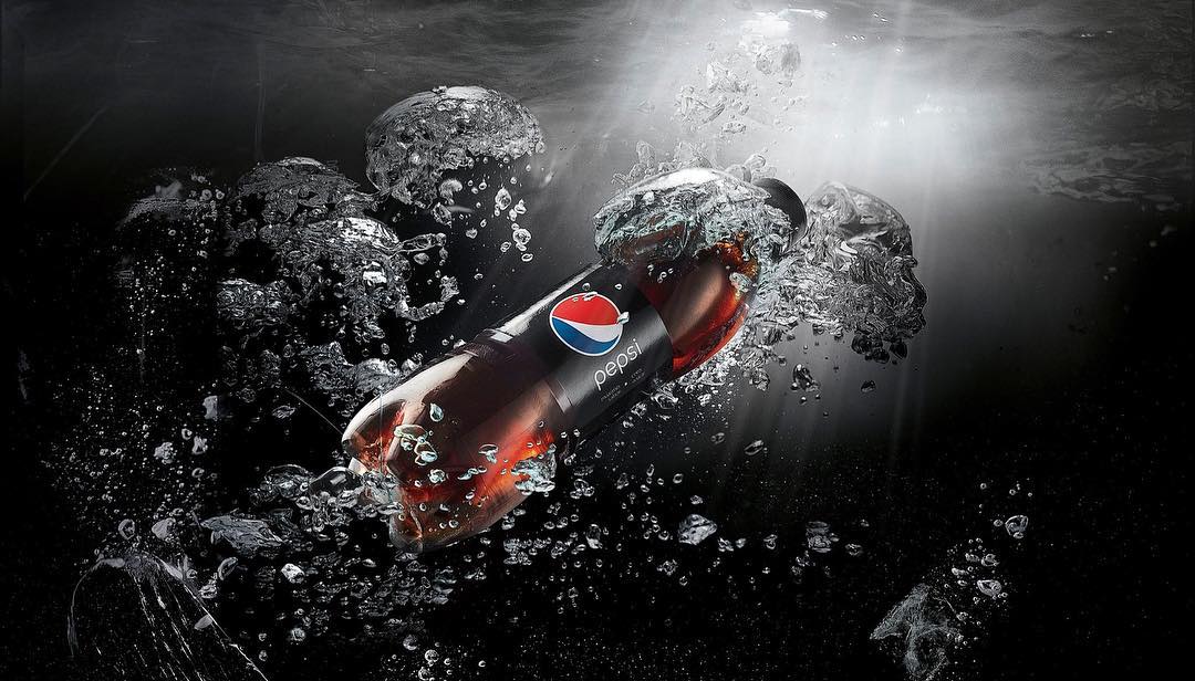 A bottle of Pepsi floats in water with air bubbles against a dark background with dramatic lighting for a refreshing beverage advertisement.
