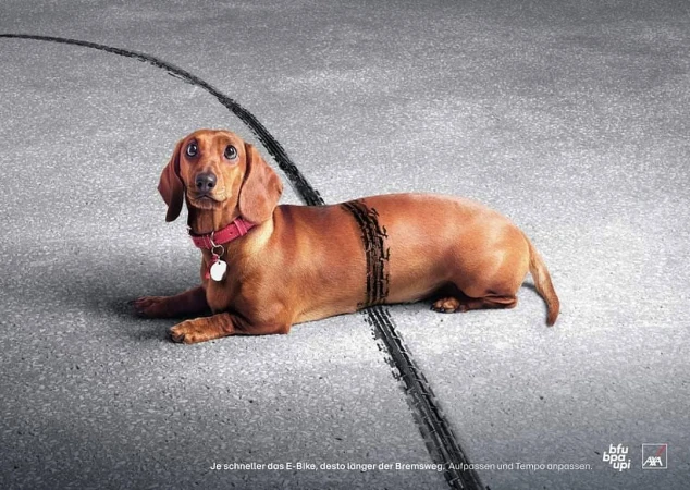 A dachshund with a red collar lies on asphalt with tire tracks across its body in a conceptual image, beside safety advertising.