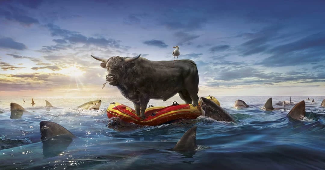 A bull stands on a raft surrounded by sharks in the ocean, with a seagull perched on its back against a blue sky with clouds.