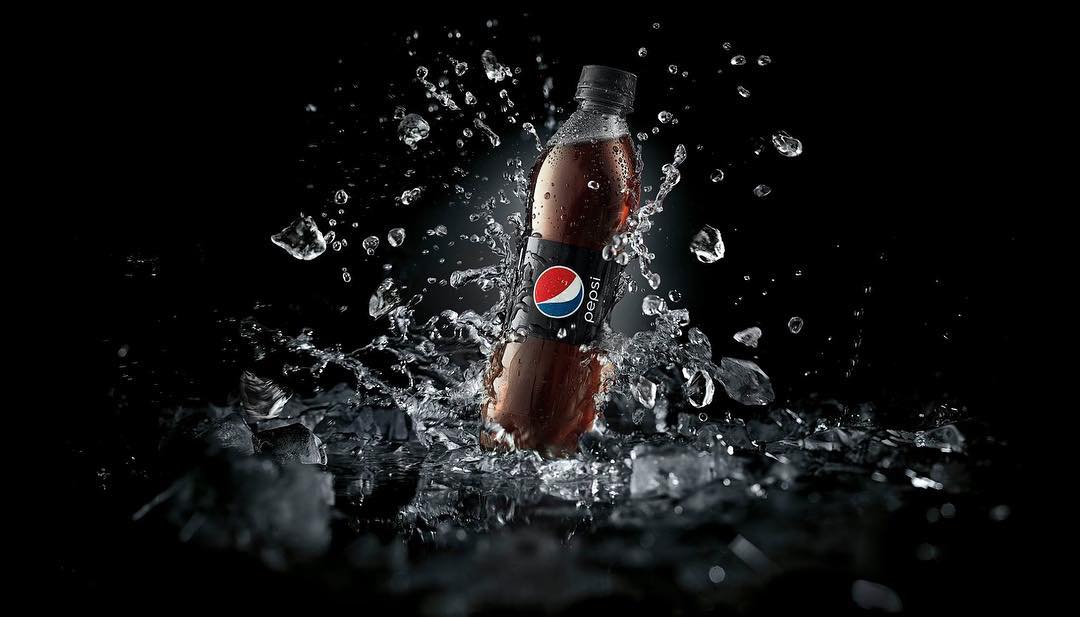 A bottle of Pepsi with water droplets and ice crystals around it is placed against a stark black backdrop, product photography.