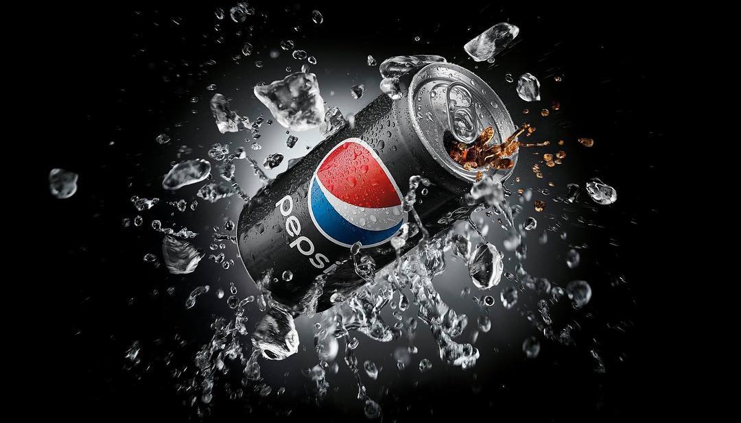 A soda can with condensation is surrounded by water droplets against a black background. The can has the Pepsi logo on it.