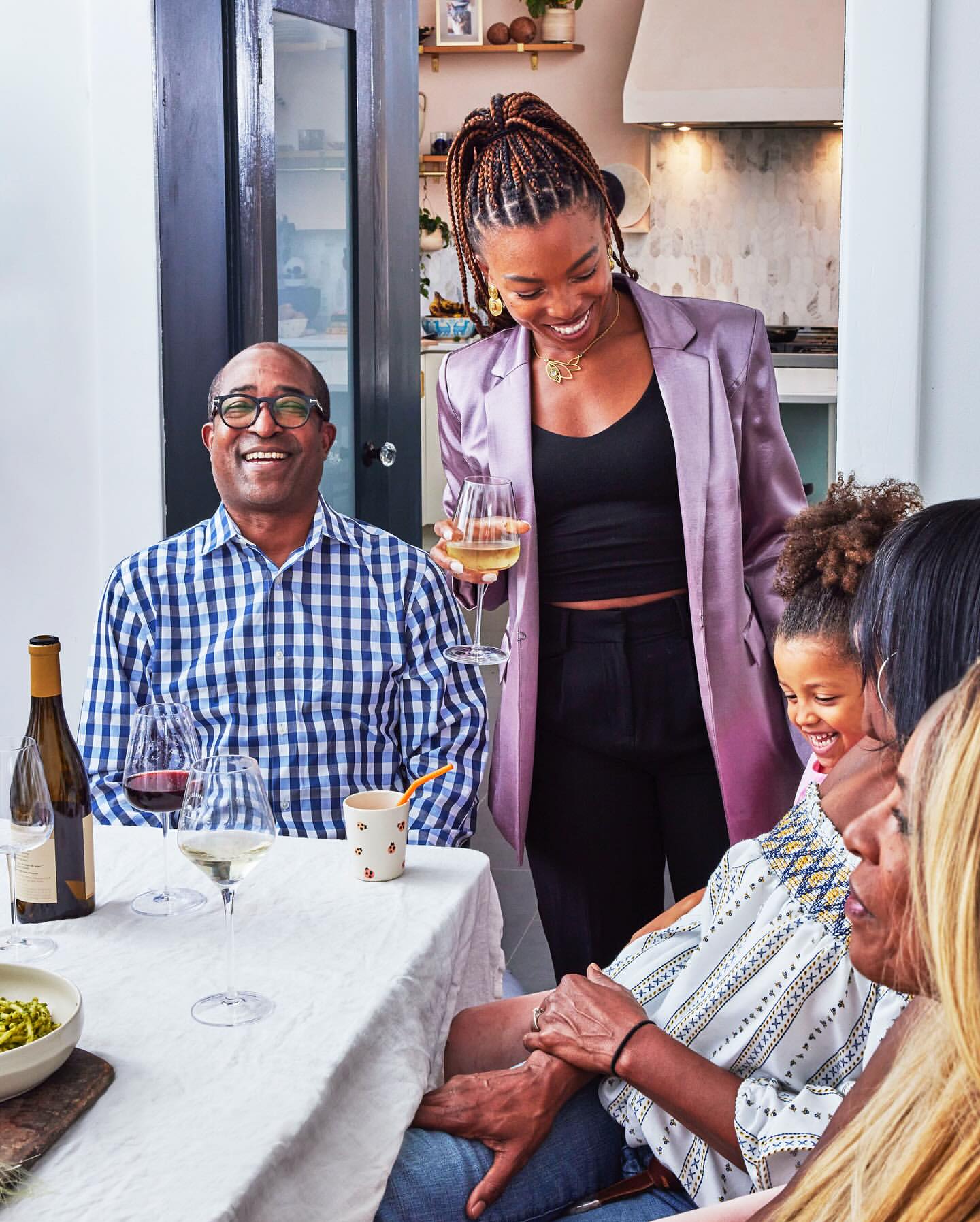 Family enjoying a meal together at home, featuring adults, a child, wine glasses, and a white tablecloth on the table.