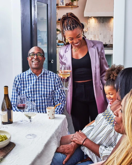 Family enjoying a meal together at home, featuring adults, a child, wine glasses, and a white tablecloth on the table.
