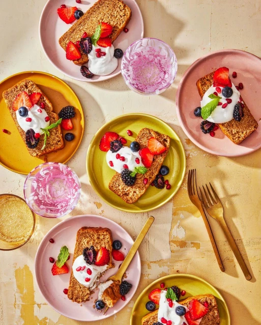 Overhead shot of individual dessert plates featuring sliced bread topped with whipped cream, assorted berries, and mint garnish.