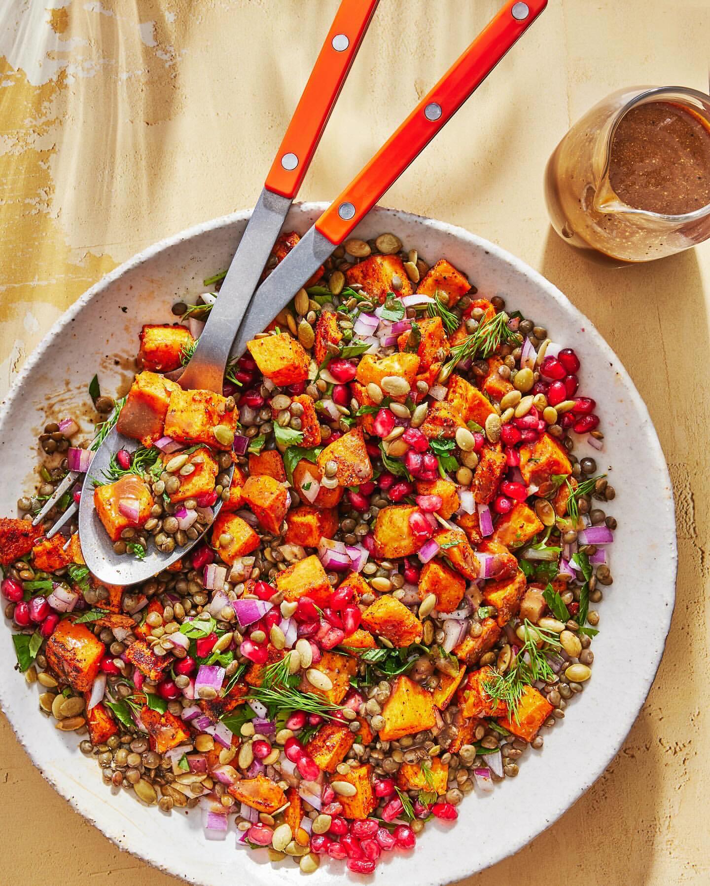 Overhead shot of a lentil and roasted sweet potato salad with red onion and pomegranate seeds, garnished with dill.