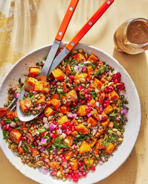 Overhead shot of a lentil and roasted sweet potato salad with red onion and pomegranate seeds, garnished with dill.