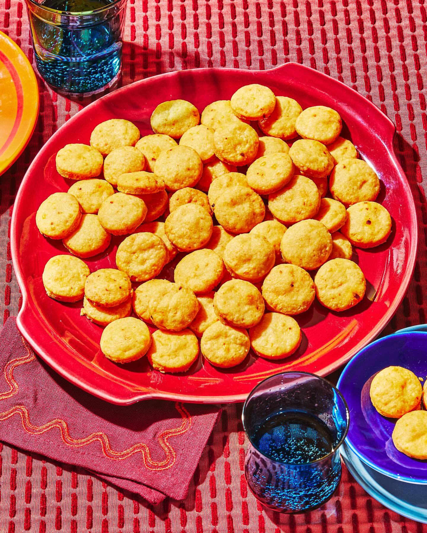 Overhead shot of a red plate filled with cheese crackers alongside a purple napkin, blue drinking glass, and red patterned tablecloth.