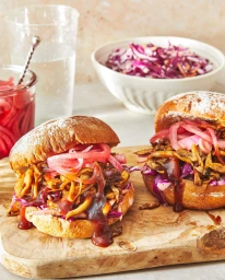 Two gourmet pulled mushroom sandwiches with pickled red onions on a wooden board, shot by Cait Bensel.