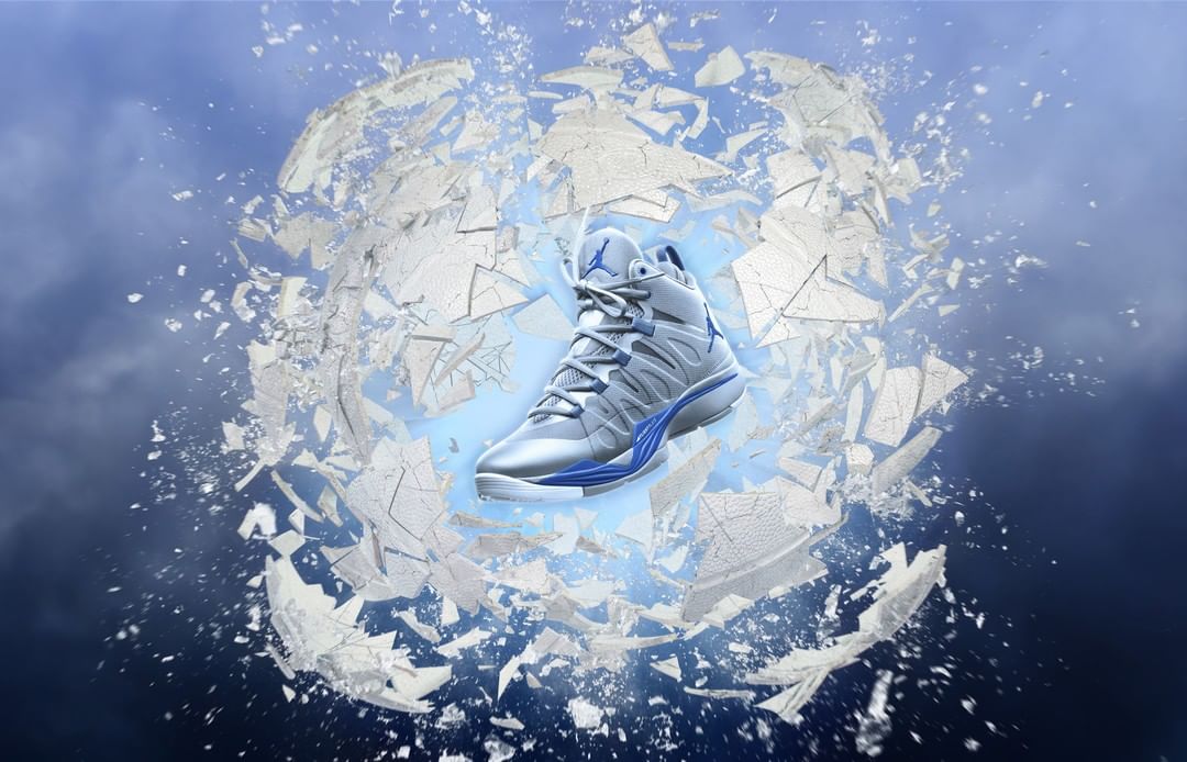 High-top silver and blue athletic shoe floats against a blue gradient background and a shattered sphere of fragmented white material.