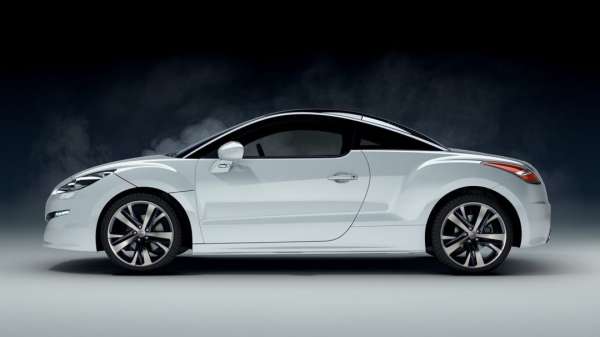 White Peugeot RCZ coupe parked in a photo studio, side view. Sleek design with black roof, stylish wheels, and blurred background.