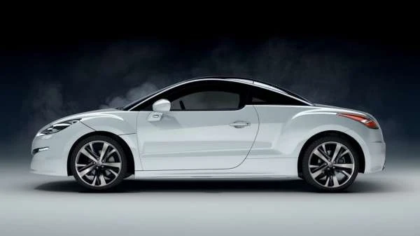 White Peugeot RCZ coupe parked in a photo studio, side view. Sleek design with black roof, stylish wheels, and blurred background.