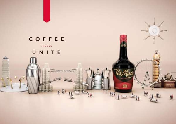 Tia Maria liqueur bottle with coffee accessories: shakers, grinders, miniature buildings and people in a product photography still life.