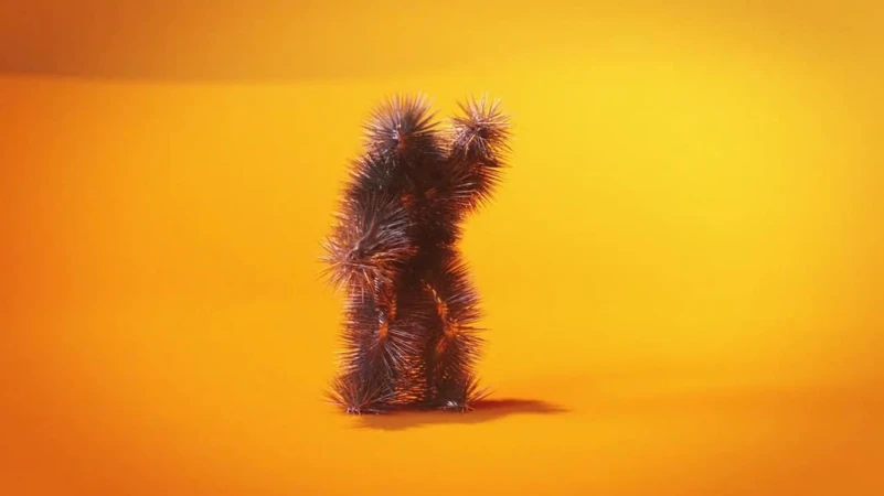 Spiky anthropomorphic figure stands in an orange-lit studio. Unique character with a textured, furry surface creating a surreal and intriguing image.