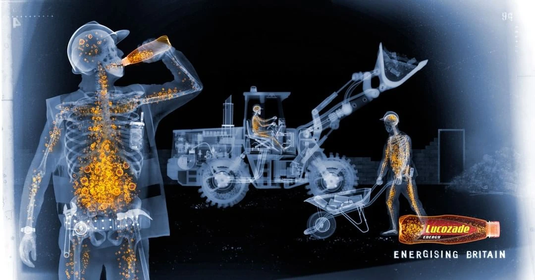 X-ray style energy drink advertisement featuring construction workers drinking Lucozade, bulldozer, and wheelbarrow against a dark background.