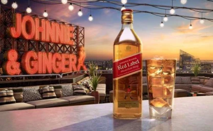 Johnnie Walker Red Label whisky bottle and a highball glass with ice on a rooftop bar at sunset.