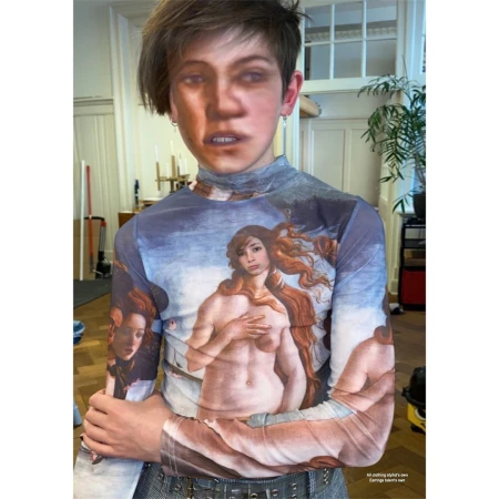 Indoor shot of a person wearing a long-sleeved top with art printed on it, posing in front of an indoor background with a neutral palette.