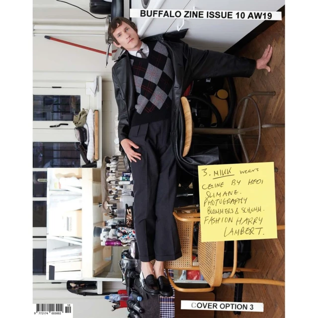 Magazine cover featuring a male model in a leather jacket, argyle sweater, and trousers. The background includes a mix of props and furniture.