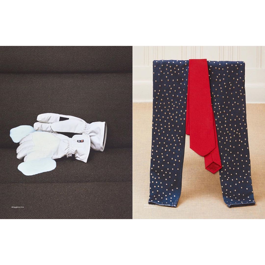 Still life featuring winter gloves on a dark brown sofa and a red necktie draped on polka dot-printed fabric over a stool.