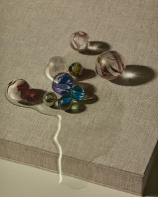 Scattered glass marbles on a textured gray surface with light casting shadows, creating a visually intriguing composition.