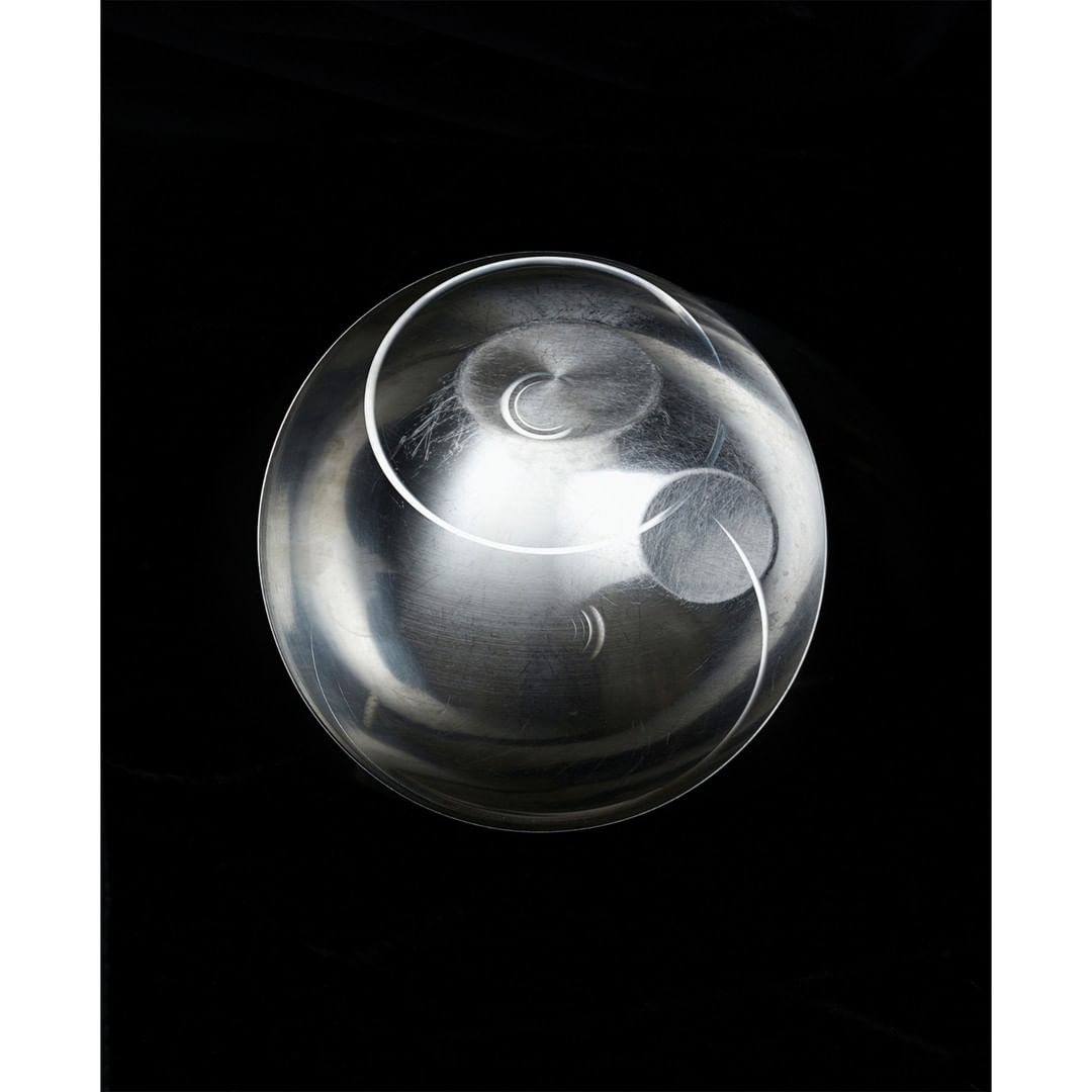 Abstract design featuring a clear glass bowl with a silver metallic interior and circular patterns against a solid black background.