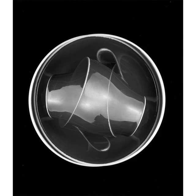 Black and white still life photograph of two reflective glass coffee cups sitting inside a clear glass saucer with a dark background.