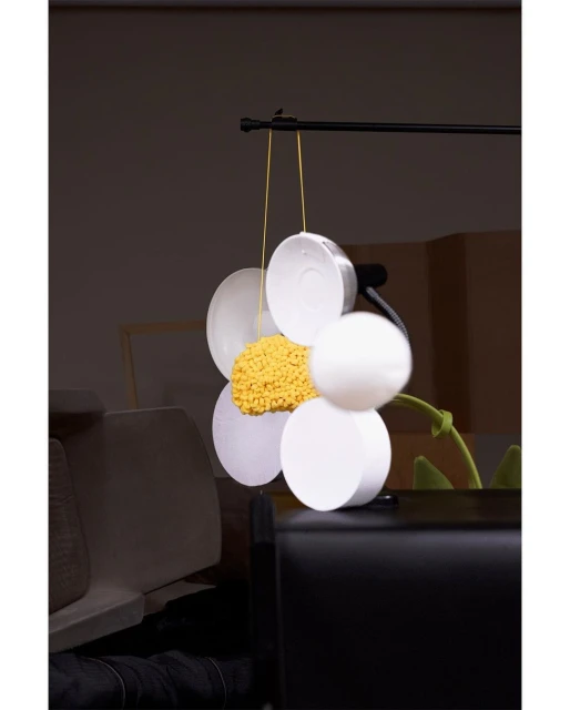 Abstract flower sculpture with white petals and yellow center suspended in an indoor setting with a blurred background.