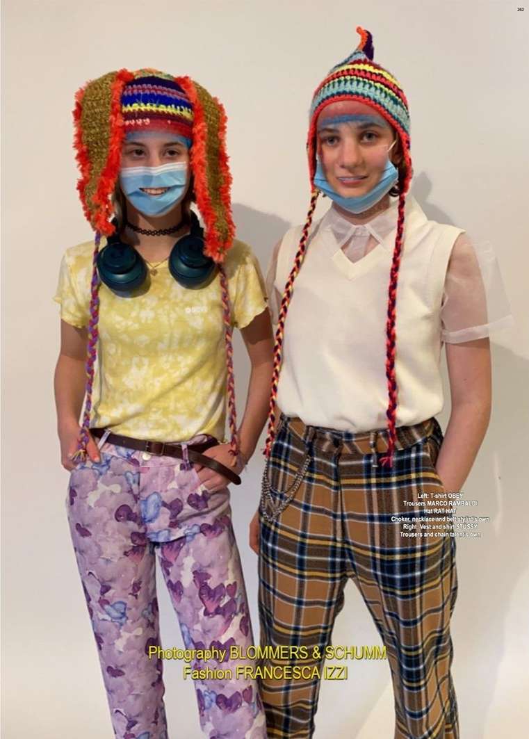 Two models wear crochet hats and face masks in an indoor fashion editorial, showcasing colorful patterns and diverse textures against a neutral backdrop.