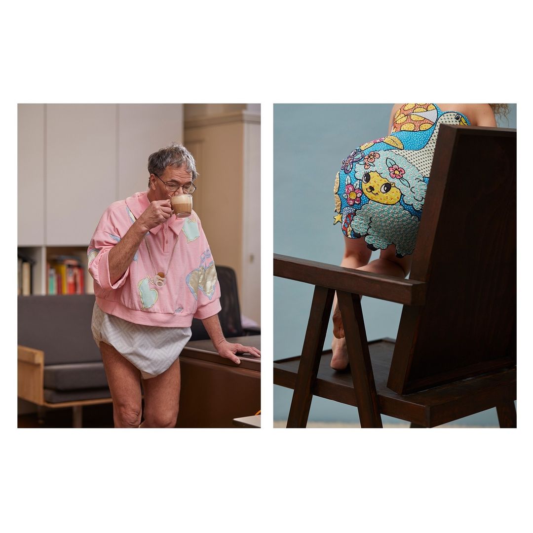 Older adult in pink top drinking coffee near sofa and bookshelves alongside a child with cartoon-printed bottoms near chair.