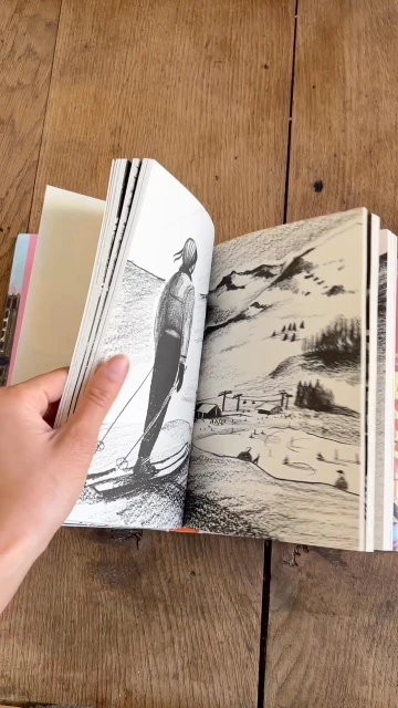Illustration of a skier going down a mountain slope in a book, captured on a wooden table, showcasing monochrome art and outdoor winter sport.