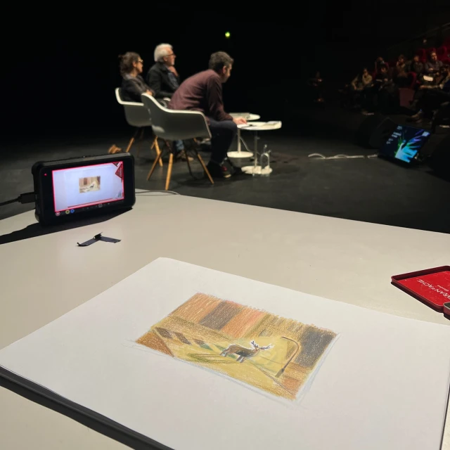 Illustration of a deer on a table in a dark room, likely part of a presentation with people in the background. Art, design, media.