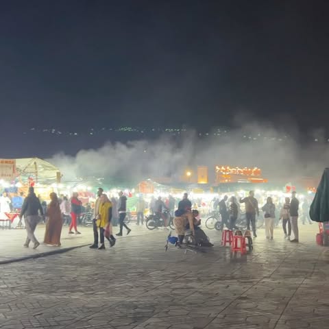 Busy night market scene with many people, food stalls, and glowing lights under a dark sky, capturing the energy and atmosphere.
