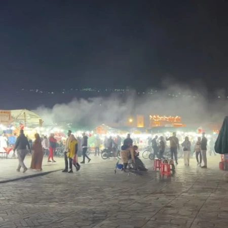 Busy night market scene with many people, food stalls, and glowing lights under a dark sky, capturing the energy and atmosphere.