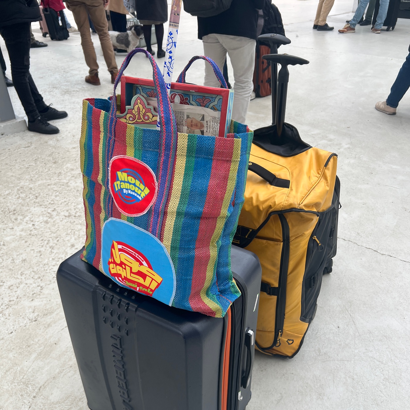 Stripped tote bag and suitcases are stacked on top of each other with blurred figures in the background, showcasing travel.