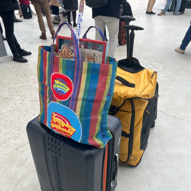 Stripped tote bag and suitcases are stacked on top of each other with blurred figures in the background, showcasing travel.